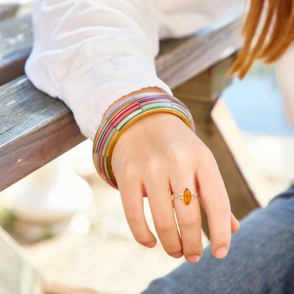Close-up of a hand resting on Papri Wood, adorned with a Multicoloured Papri Wood Bangle and an amber ring, against a backdrop of a white shirt and blue jeans.
