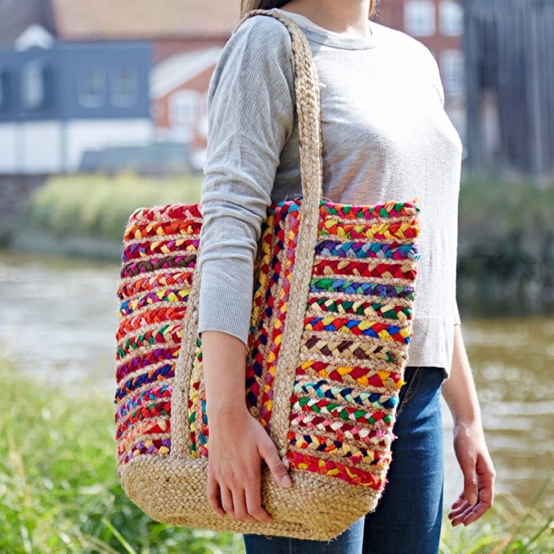 A person outdoors holds the Recycled Cotton and Jute Tote Bag, featuring a braided design and natural fiber straps—beautifully handmade for Fair Trade.