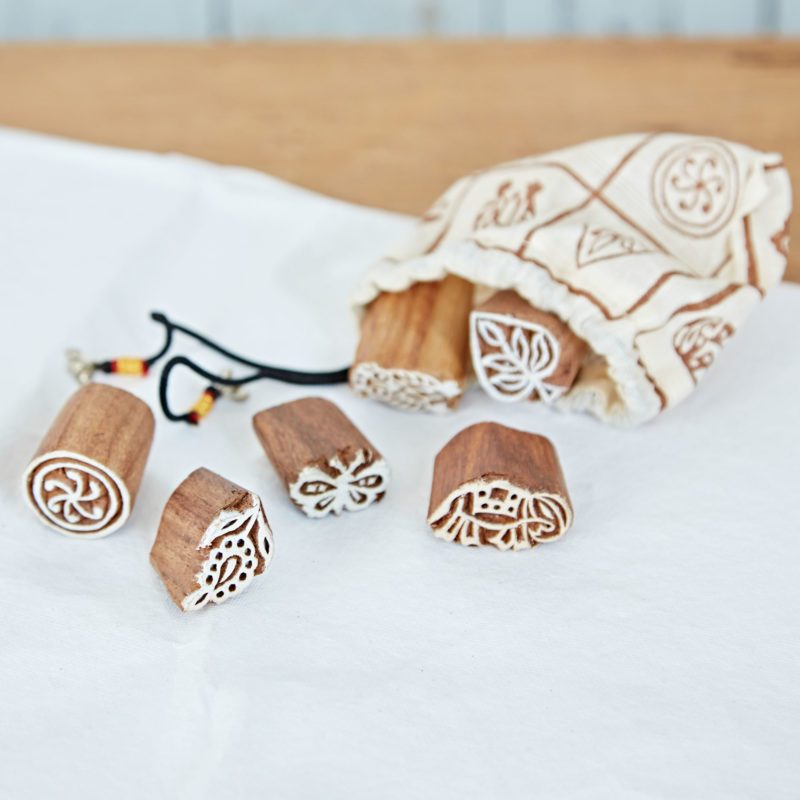 Six Assorted Design Wooden Printing Blocks with intricate patterns are displayed on a white surface beside a patterned drawstring bag, highlighting the artistry of traditional wooden printing blocks.