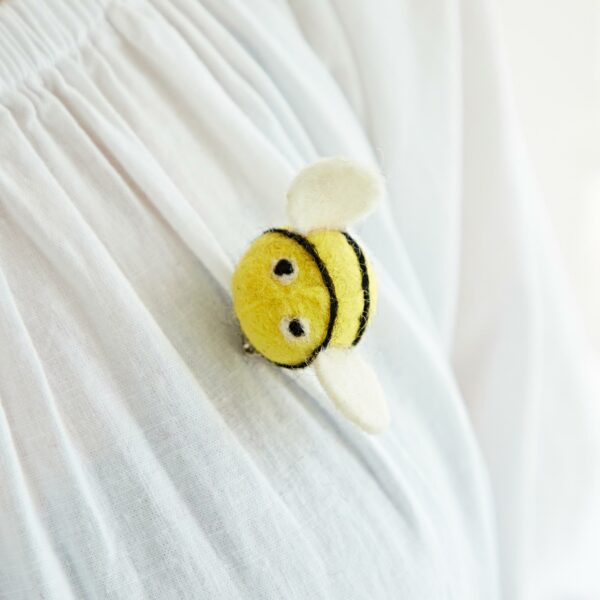 A Felt Bee Brooch, featuring small black stripes and white wings, is pinned to a crisp white garment.