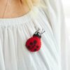 A close-up of a Pack of 3 Felt Ladybird Brooches with black dots, pinned on a woman's white blouse with gathered neckline detail.