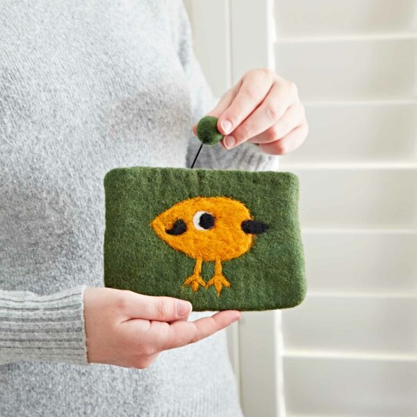 Person holding a Felt Bird Purse, made of wool, standing in front of white shutters.