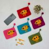 Five colorful Felt Bird Purses, a plant in a black pot, a smartphone, a pair of train tickets, and two coins arranged on a white surface.