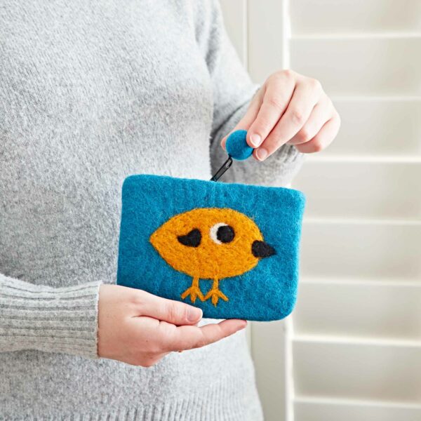 A person is holding a Felt Bird Purse in front of white shutters.