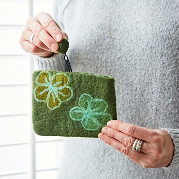 A person holds the Felt Flower Purse, a small green accessory with colorful floral embroidery, against a light background.