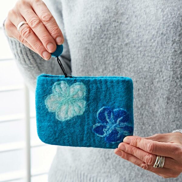 A person cradles the Felt Flower Purse, its charming blue felt adorned with delicate floral designs and featuring a simple button closure.