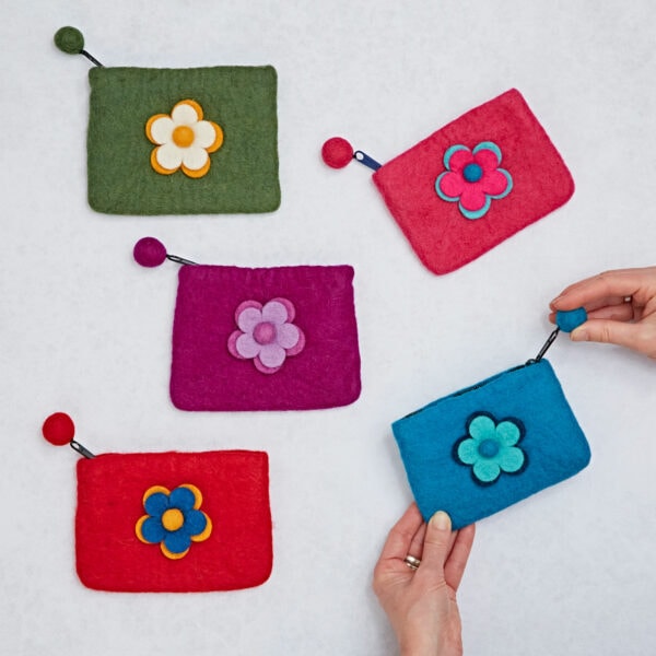 A set of five vibrant Felt Daisy Purses with zip closures is showcased on a light surface, with the blue purse held in hand.