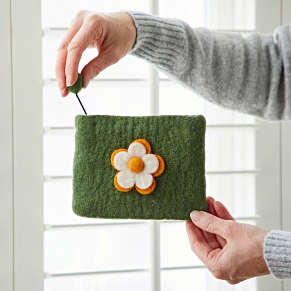 Hands holding a Felt Daisy Purse, made of green fabric with a white and orange daisy design; one hand gently unzips it.