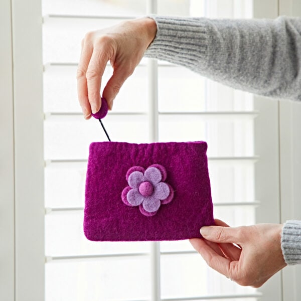 Hands holding the Felt Daisy Purse, a small purple felt purse with a charming daisy design, set against white window blinds.