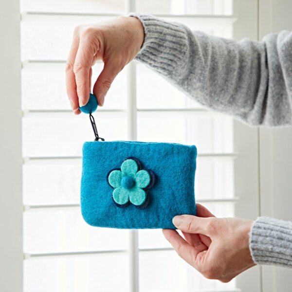 Near a window, someone holds the Felt Daisy Purse, a blue felt coin purse beautifully adorned with a daisy design.