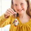 A smiling child in a yellow top holds up a Felt Penguin Keyring made of felt, proudly showing it to the camera.