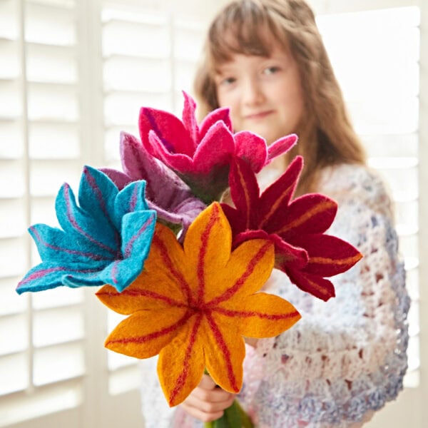 Someone holds a vibrant Felt Flower bouquet, its vivid colors standing out against pristine white shutters.
