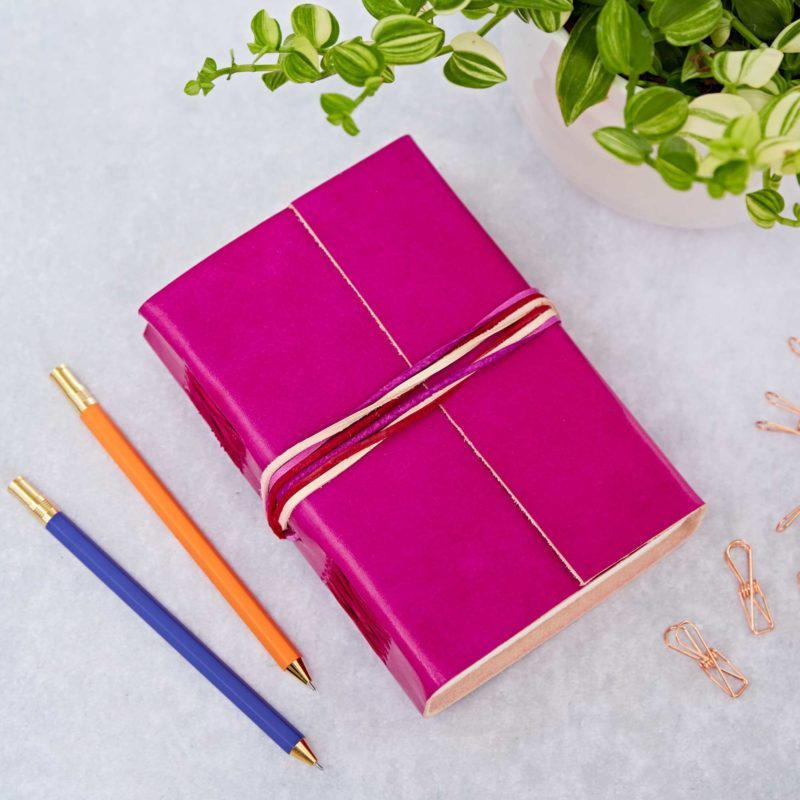 A handmade cerise leather journal with a three coloured string.
