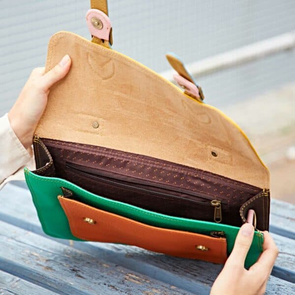 A person opens the Multicoloured Recycled Leather Satchel to reveal its vibrant suede interior, zip-fastened compartment, and multiple pockets.