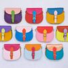 Ten vibrant leather handbags, such as the Multicoloured Saddle Crossbody Bag, feature buckle closures and are artfully arranged in a grid against a light background.
