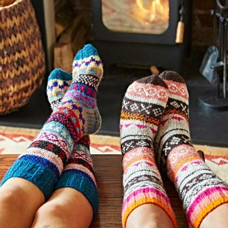 Two people wearing colorful socks in front of a fireplace.