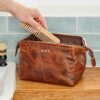 A person using a comb with a Personalised leather wash bag. The unique structured frame of this wash bag allows it to open widely and stay open.