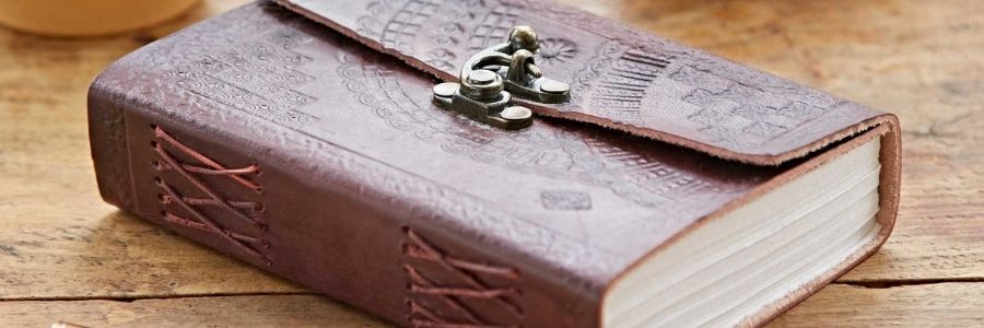 A closed brown leather journal with embossed patterns and a metal clasp rests on a wooden surface—a thoughtful pick from the Fair Trade Father's Day Gift Guide.