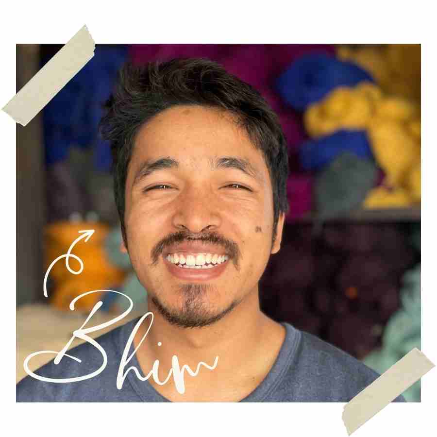 A man smiling in front of a bunch of yarn during his trip to Nepal.