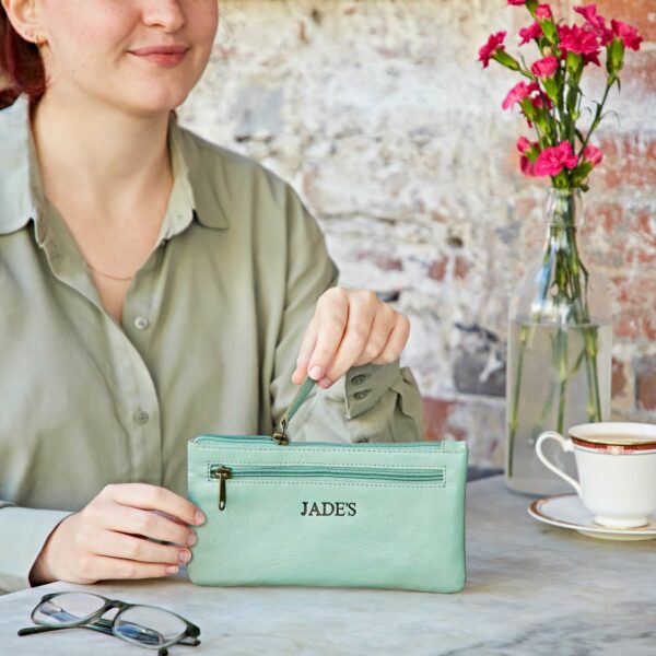 A woman sitting at a table holding a Personalised Leather Clutch Purse.