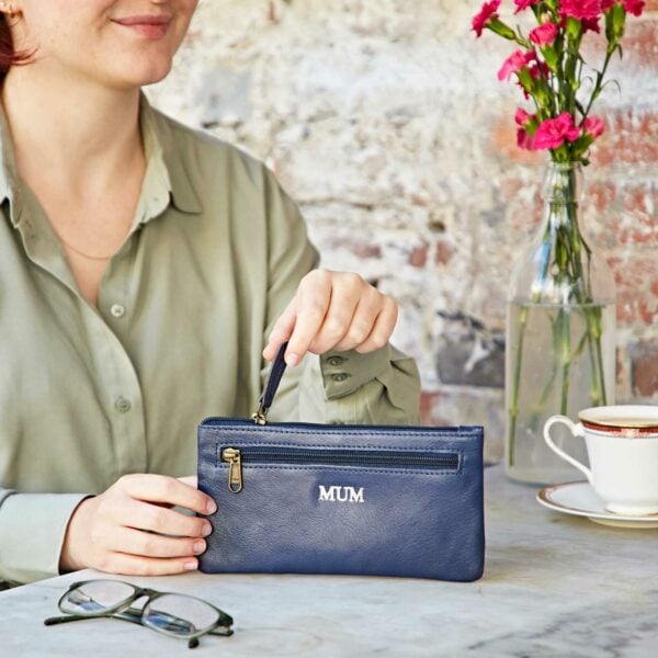 A woman sitting at a table holding a Personalised Leather Clutch Purse.