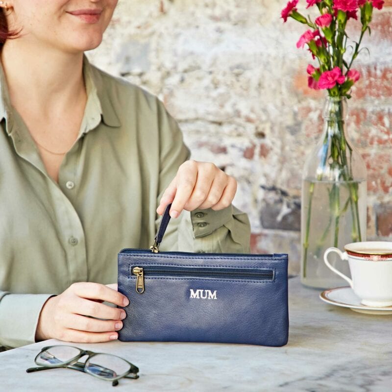 A woman sitting at a table holding a Personalised Leather Clutch Purse.