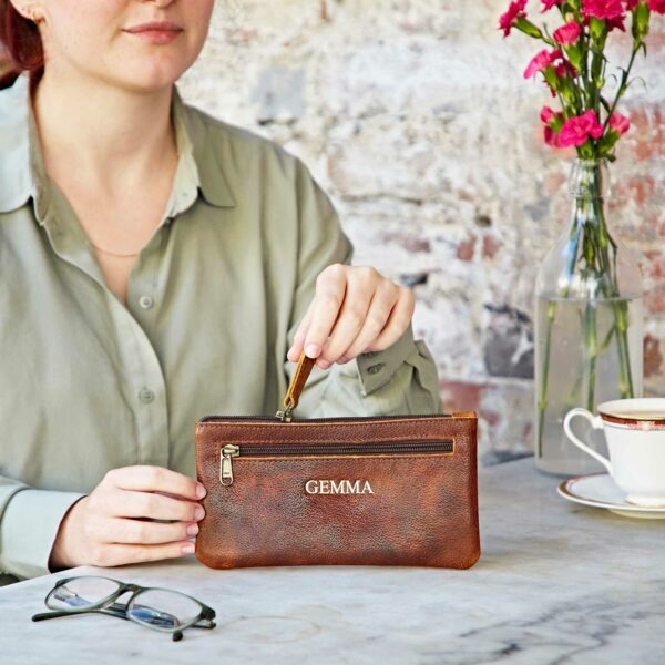 A woman is sitting at a table holding a Personalised Leather Clutch Purse.