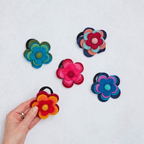 A hand delicately presents a Felt 4 Flower Hair Band against a pristine white background.