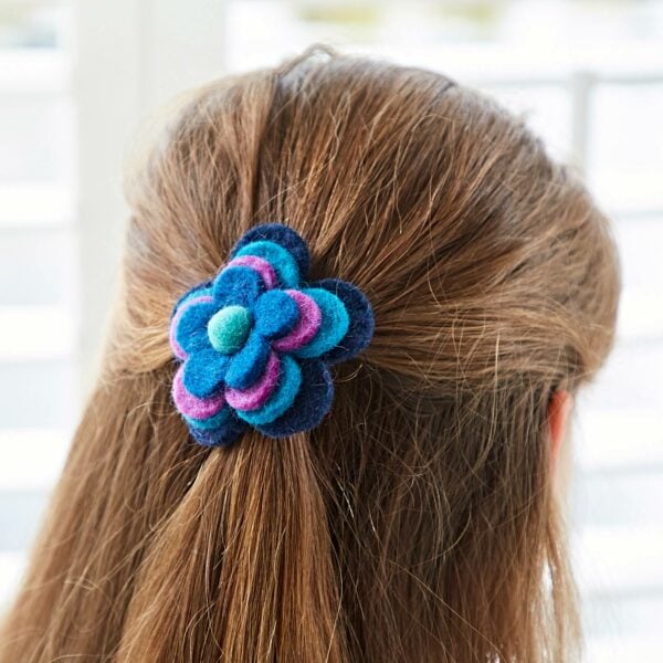 A person with brown hair sports a stylish Felt 4 Flower Hair Band in blue and purple, viewed from behind against a blurred background.