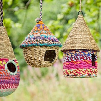 Three colourful woven birdhouses hanging from branches.