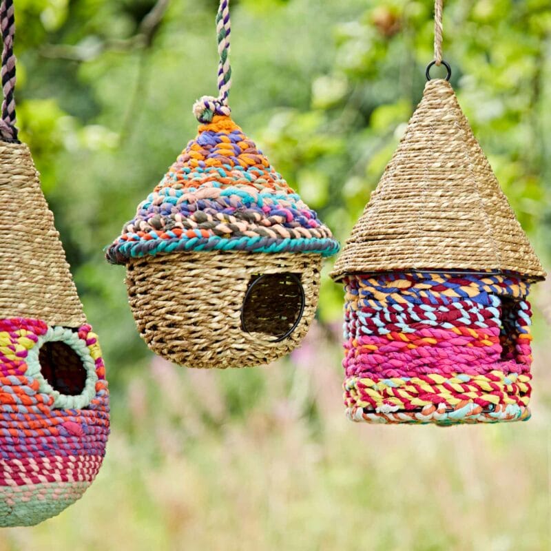 Three colourful woven birdhouses hanging from branches.