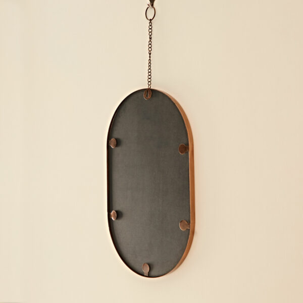A Darpan Oval Antique Copper Hanging Chain Wall Mirror, suspended against a cream-colored wall.