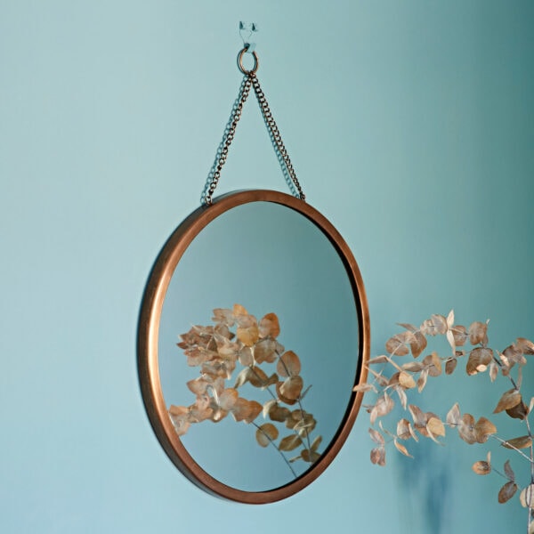 A **Arasa Round Antique Copper Hanging Chain Wall Mirror** adorns a blue wall, reflecting dried foliage.