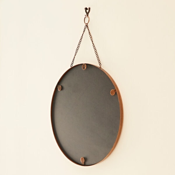 An Arasa Round Antique Copper Hanging Chain Wall Mirror hangs from a chain mounted on a wall.