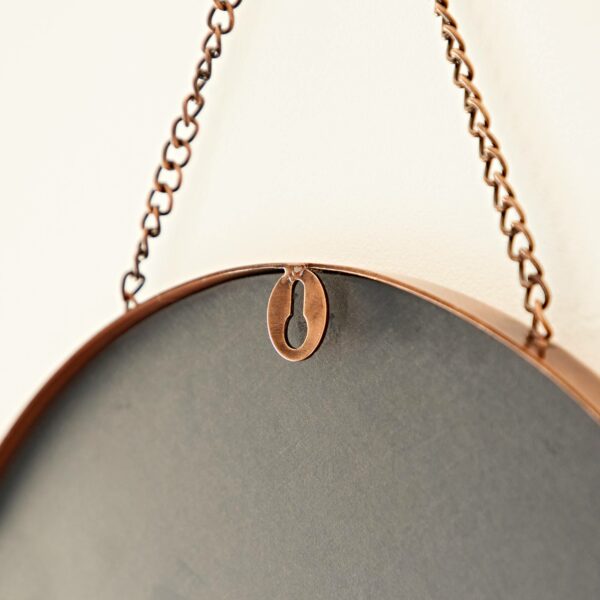 A round metal object with an antique copper finish is hanging on a wall, suspended by a hanging chain. The image shows a close-up of the back, focusing on the hanging mechanism of the Arasa Round Antique Copper Hanging Chain Wall Mirror.