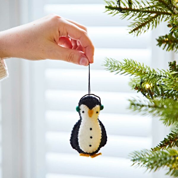 A person is holding a Felt Penguin In Earmuffs Christmas Decoration on a Christmas tree.