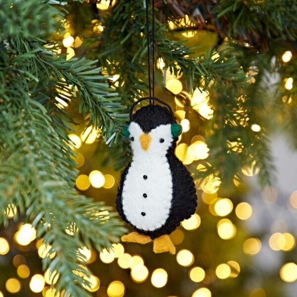 A Felt Penguin In Earmuffs Christmas Decoration, hanging from a tree.