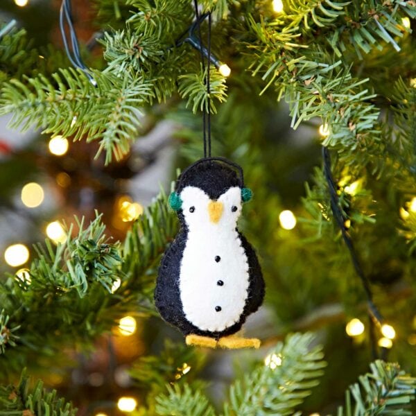 A Felt Penguin In Earmuffs Christmas Decoration, hanging from a tree.