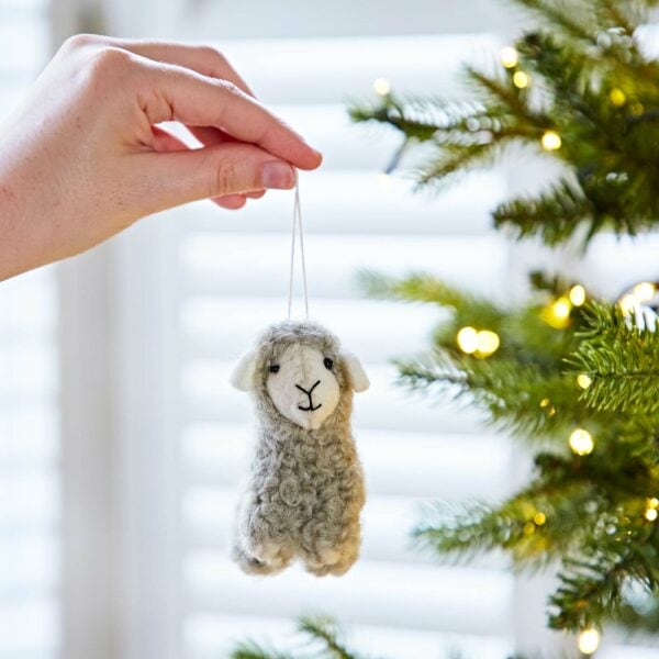 A person holding a felt sheep Christmas decoration on a tree.