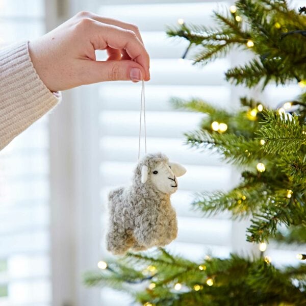 A person adorning a Felt Sheep Christmas Decoration on a tree.