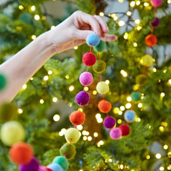 A person is holding a Handmade Multicoloured Felt Ball Garland on a christmas tree.