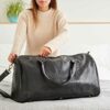 A woman holding a Personalised Large Black Leather Weekend Holdall on a bed.