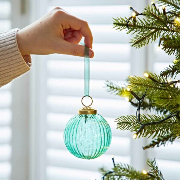 A person is holding an Ira Glass Baubles on a Christmas tree.
