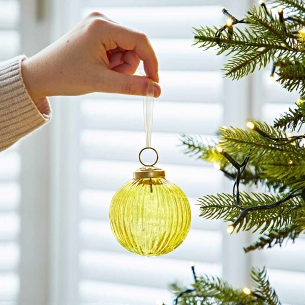 Ira Glass holding a yellow Ira Glass Bauble in front of a Christmas tree.