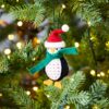 A Felt Penguin In Santa Hat Christmas Decoration hangs from a Christmas tree.