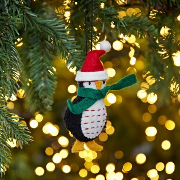 A Felt Penguin In Santa Hat Christmas Decoration hanging from a Christmas tree.
