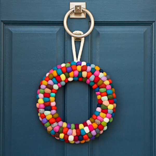 A Felt Multicoloured Wreath, vibrant in its woolen hues, adorns a blue door beside a silver knocker.