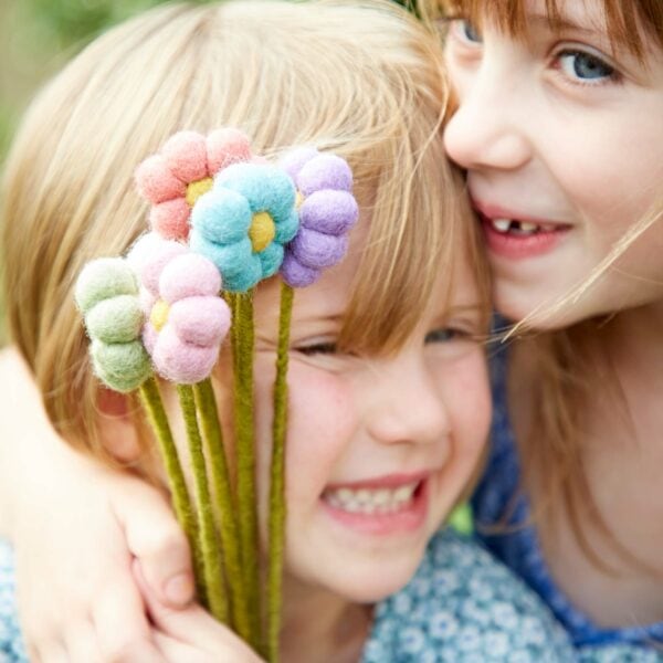 Two little girls hugging each other while holding a Pack of 6 Felt Handmade Flower Bouquet.