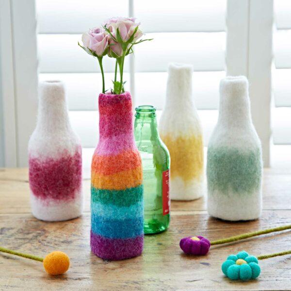 Handmade felt bottle vases with colourful flowers on a wooden table.