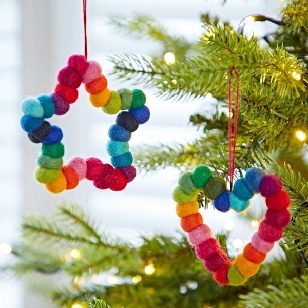 Two Felt Multicoloured Hanging Decorations—one shaped like a star and one like a heart—hang on a Christmas tree decorated with twinkling fairy lights.